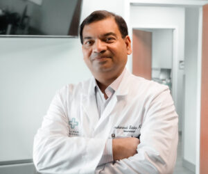 Dr. Siddiqi standing with arms crossed in bright waiting room with white lab coat.